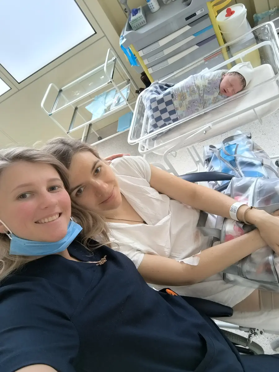 Две женщины рядом у больничной кровати; позади них в кроватке лежит новорождённый
